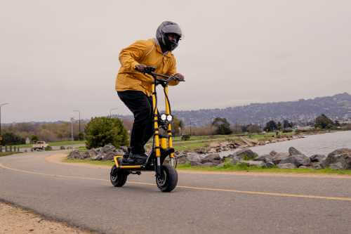 Kaabo Wolf King electric scooter - man riding scooter, tucked down to right of frame, lgiths on, can see road and water