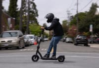 Apollo Air electric scooter - man riding scooter through intersection, to left, side view