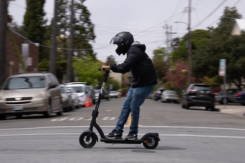 Apollo Air electric scooter - man riding scooter through intersection, to left, side view
